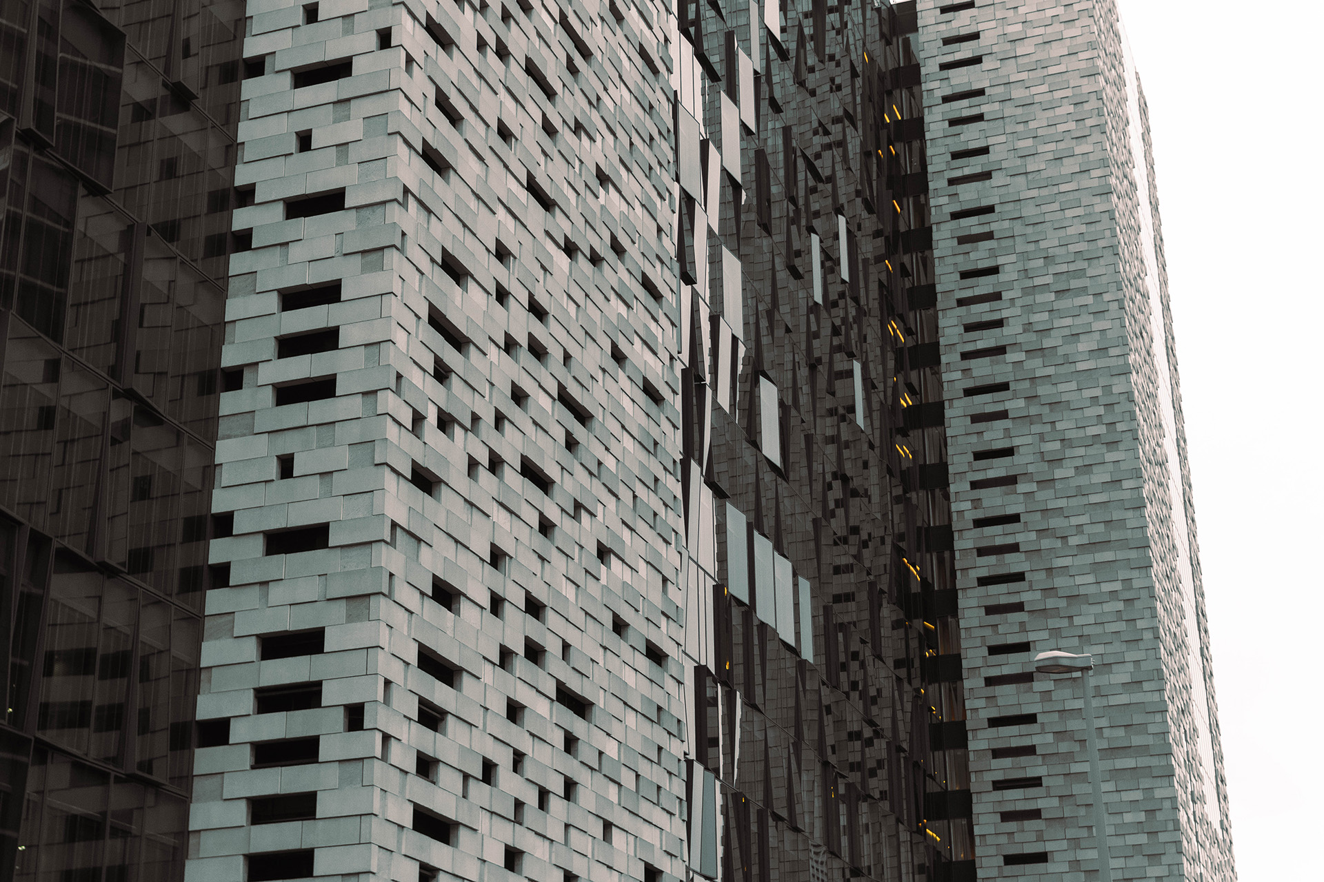 Photograph of a close-up of a tall contempory building's concrete and glass facade, made up of concrete slabs and window panes placed chaotically.